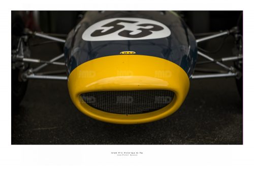 Vue de face d'un véhicule de course de collection Lola  vert foncé et jaune dans son stand avant sa course au Grand Prix de Pau Historique