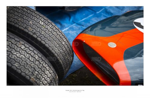 Vue de face d'un véhicule de course de collection vert foncé et orange avec deux pneus course dans son stand avant sa course au Grand Prix de Pau Historique