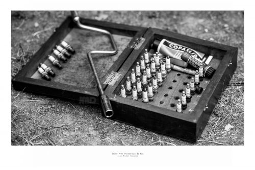Vue d'une boite en bois, posée à même le sol contenant des bougies et divers outils moteur, grand prix de Pau